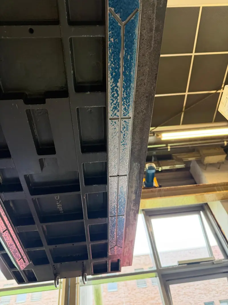 Cara inferior de una pieza larga colgada de la grúa, con la guía marcada en azul.