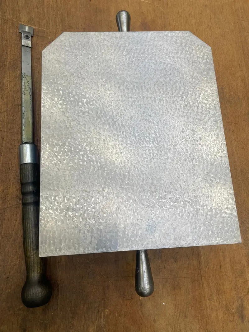 Placa rasqueteada con las esquinas achaflanadas; al lado, dos rasquetas manuales.