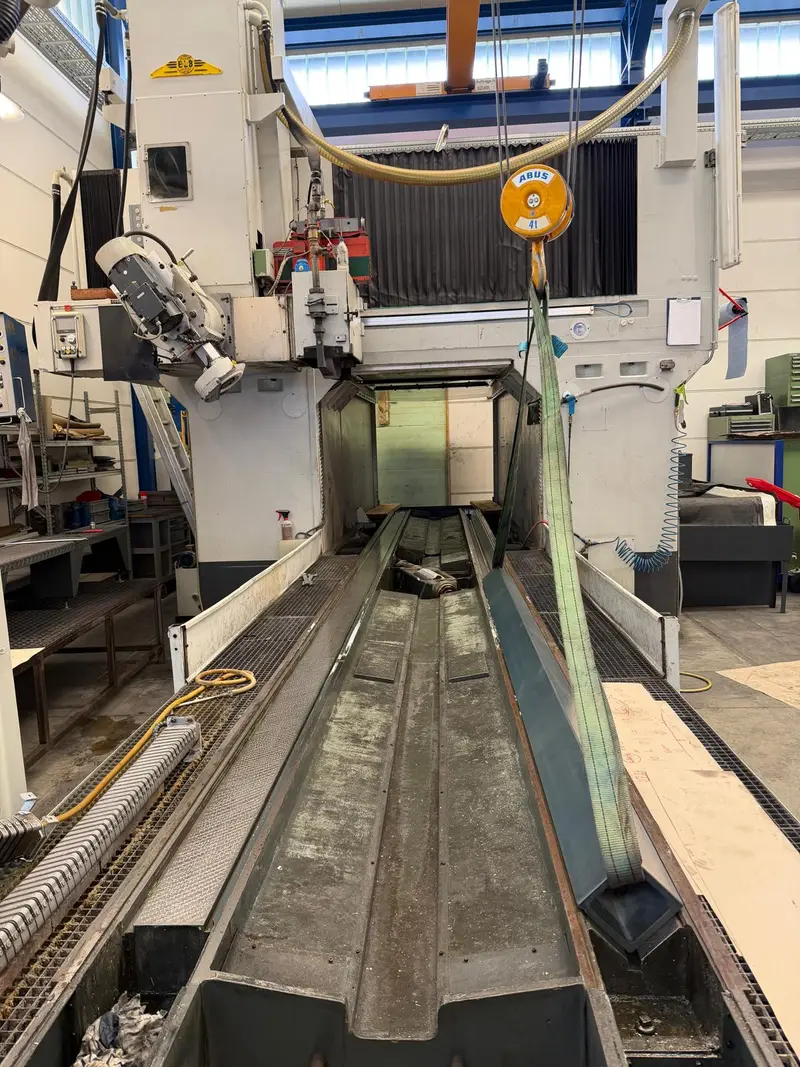 Bancada larga bajo el pórtico de la máquina; una guía cuelga de una eslinga.