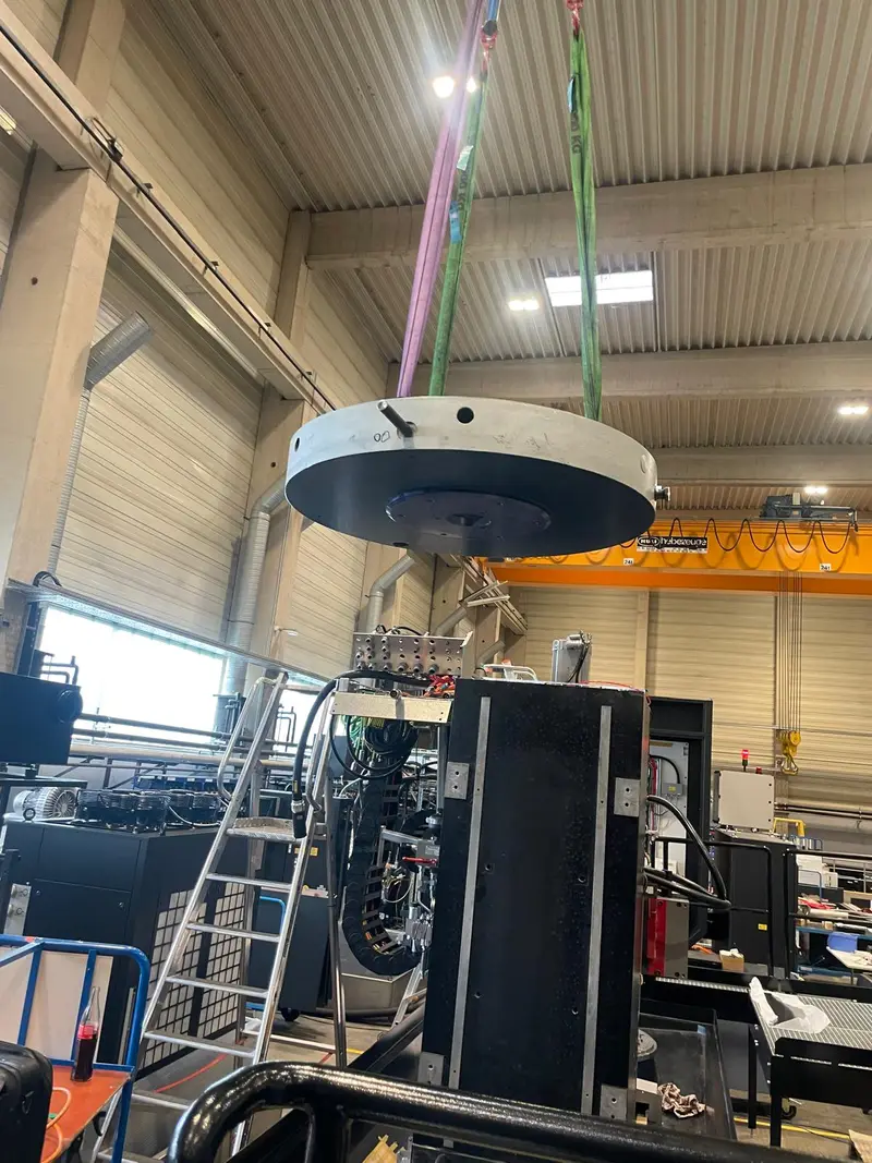 Mesa giratoria colgada de la grúa sobre la máquina, en una nave alta.