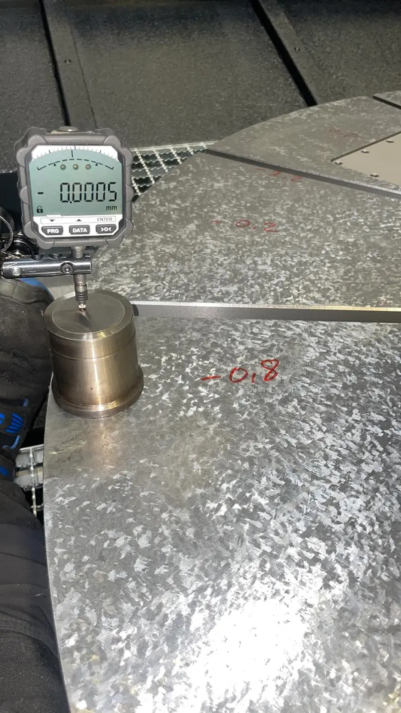 Reloj comparador digital en su soporte sobre la superficie plana rasqueteada de una mesa giratoria; al lado, un valor escrito con rotulador rojo.