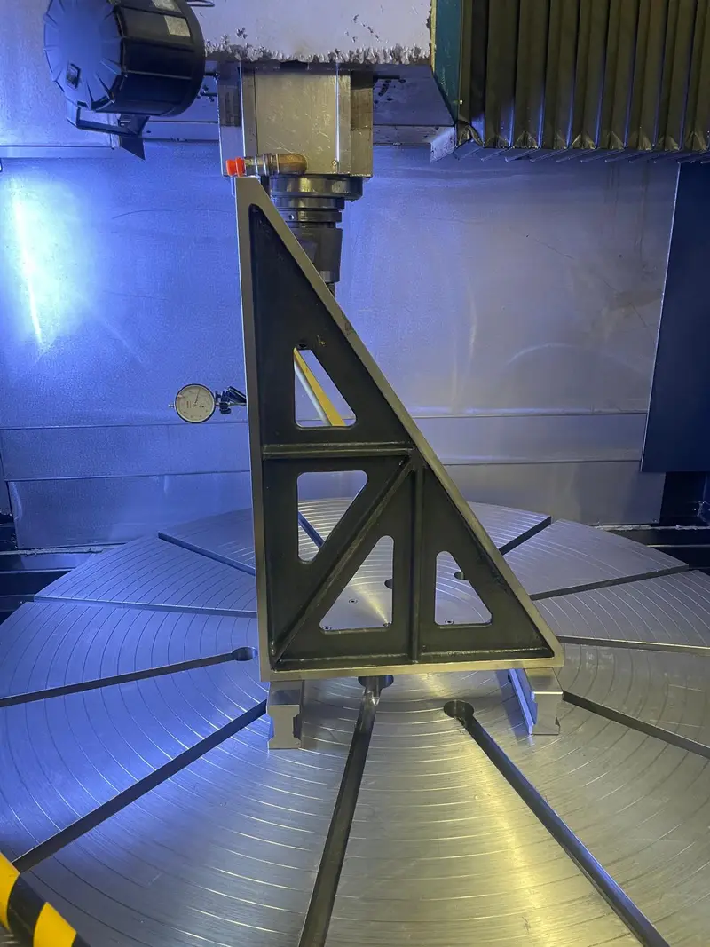 Escuadra de comprobación triangular sobre la mesa giratoria de una máquina; en el husillo principal, un reloj comparador.
