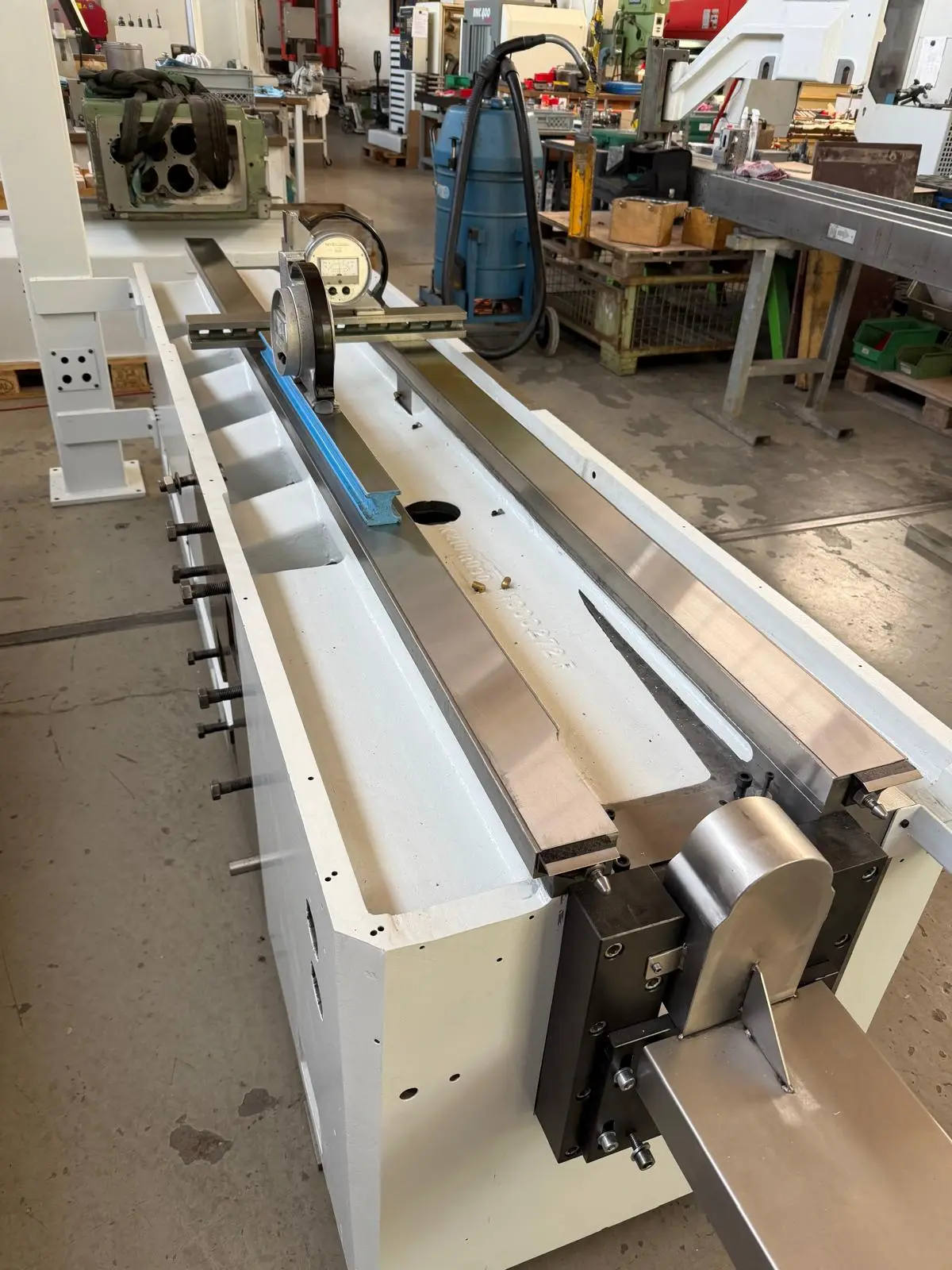 Machine bed painted white on a shop floor, with a bridge carrying an electronic level across the ways.