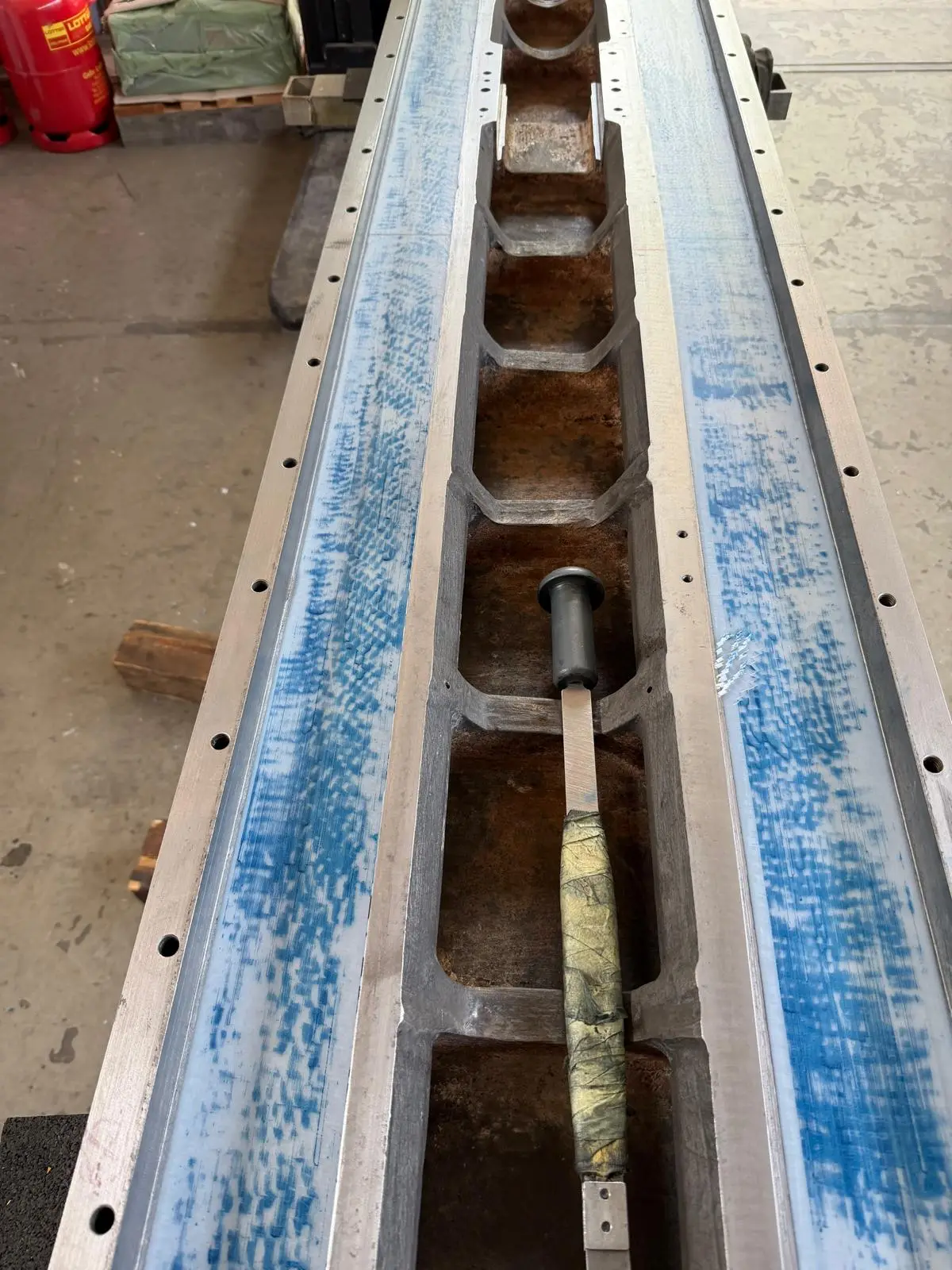 Long bed out of the machine, both ways spotted in blue. A hand scraper with a taped handle lies ready in the middle.