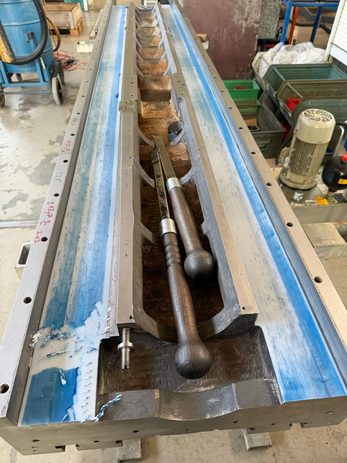 Long machine bed with both ways spotted in blue. Measuring points are marked in red along the edge, and two hand scrapers with ball handles lie in the middle.