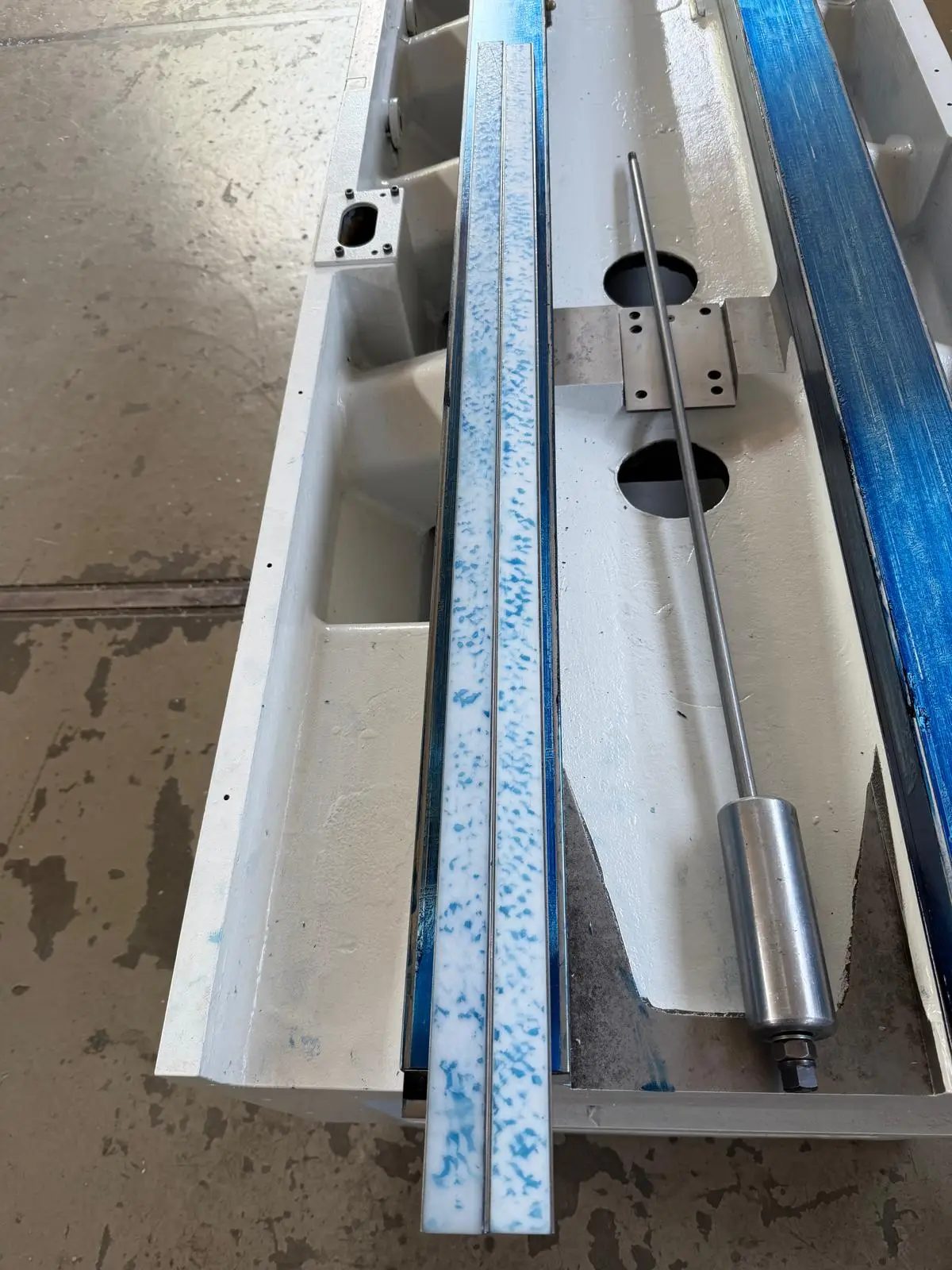 Machine bed painted white: a narrow strip with blue contact, the fully spotted way on the right, a piston rod in between.