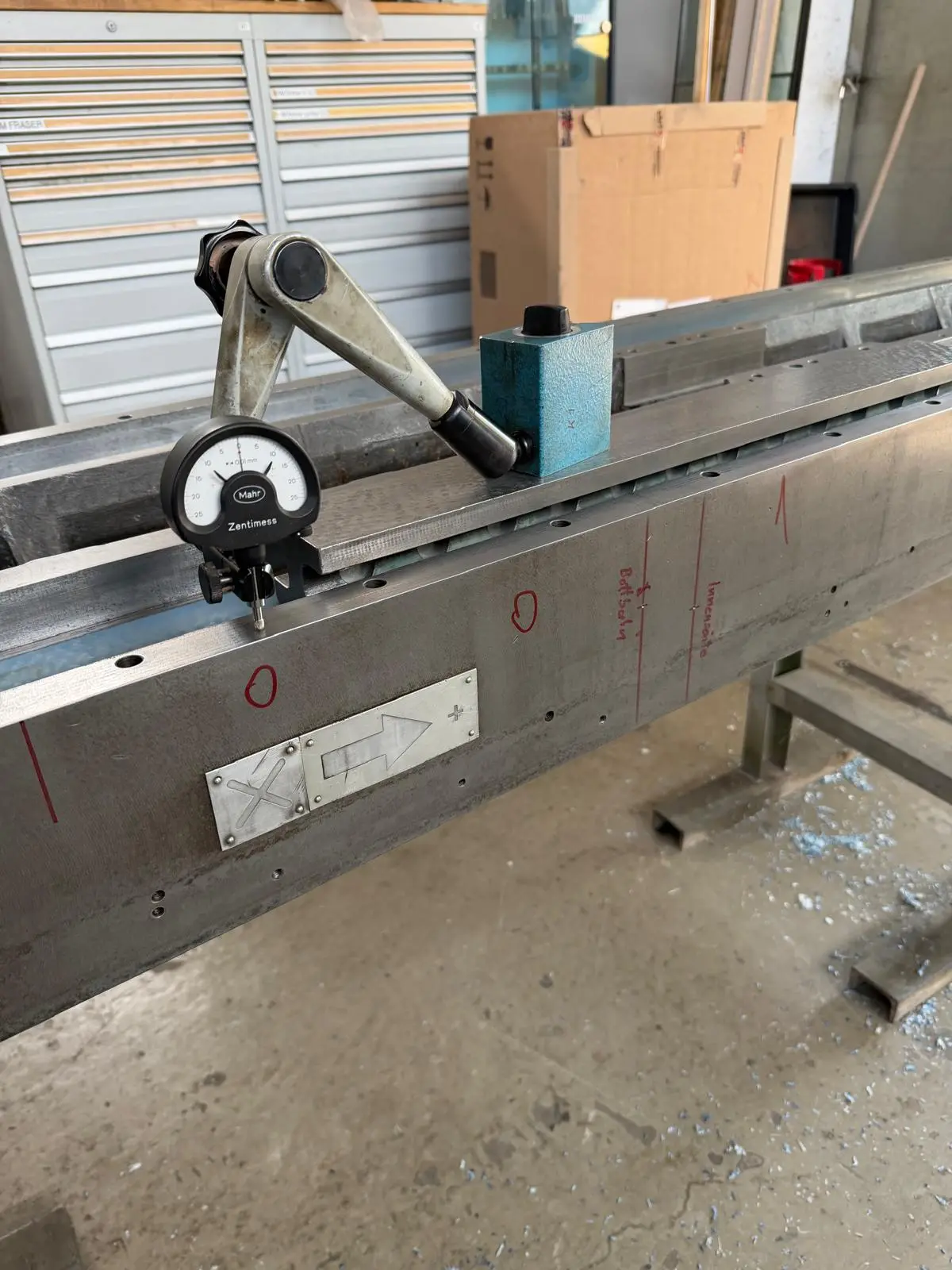 Mahr Zentimess dial indicator on a magnetic base, set against the edge of a machine bed. Measuring points are marked and labeled on the casting in red marker.