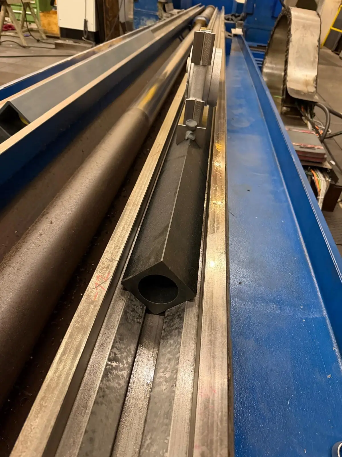 Black, hollow square straightedge in the way of a long, blue-painted machine bed. At the far end sits an aluminum holder with adjusting screws.